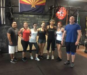 Group of people smiling at the gym with an Arizona state flag above them