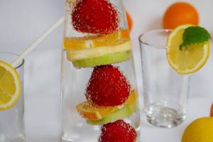Glasses of water with slices of lemon, lime, orange, and full strawberries